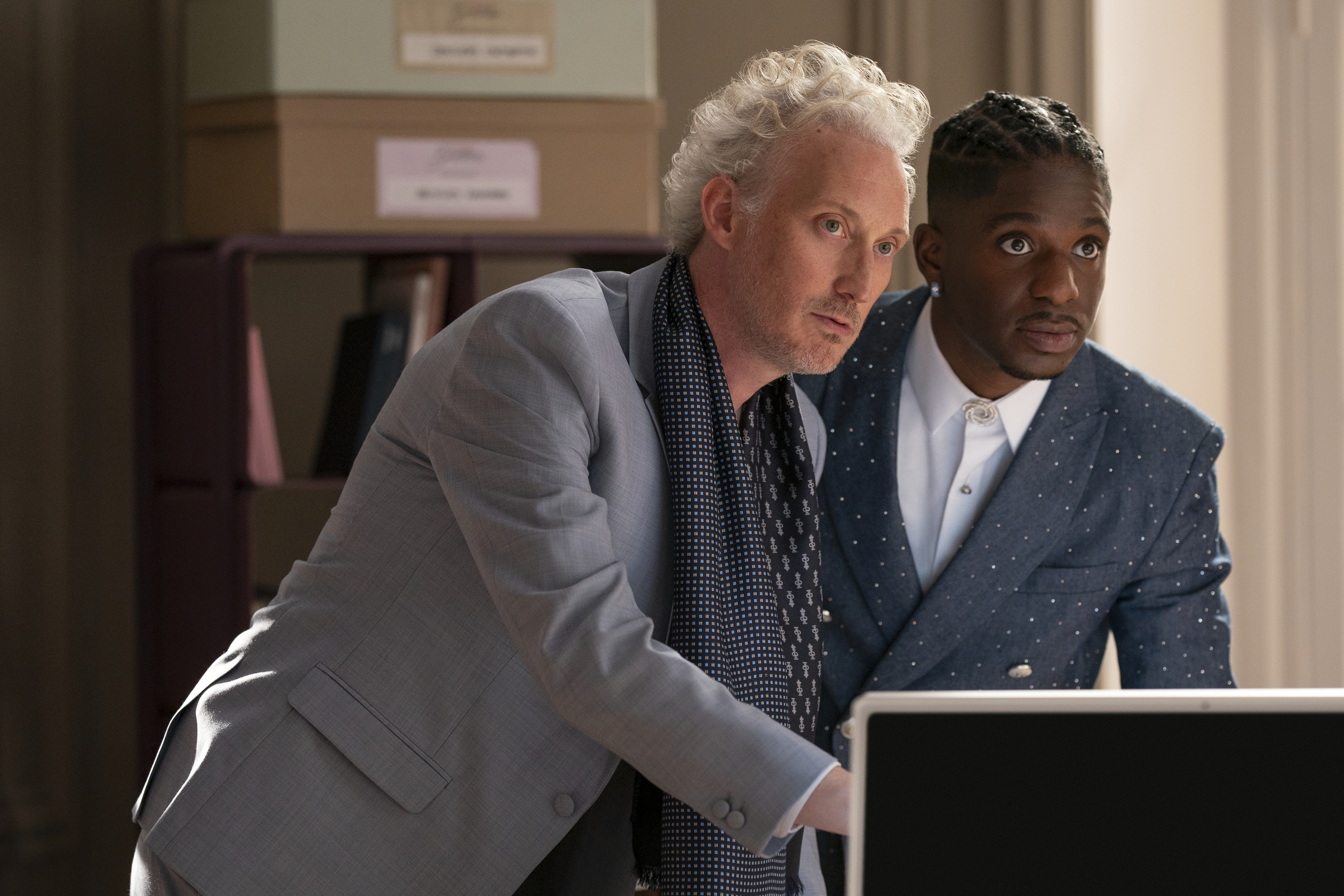 luc and julien wearing suits snoop around a computer in a still from emily in paris season 5