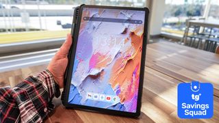 A person holding a TCL NXTPAPER 11 Plus tablet at a table with a Tom's Guide Savings Squad deals badge