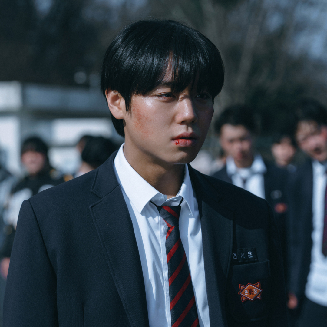 A boy with a bruised face (Park Ji-hoon as Yeo Si-eun) stands in front of a blurred crowd, in 'Weak Hero Class 2.'