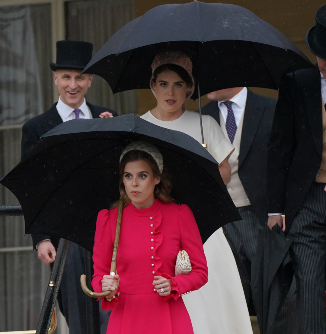 Princess Eugenie and Princess Beatrice walking down a staircase in dresses holding umbrellas