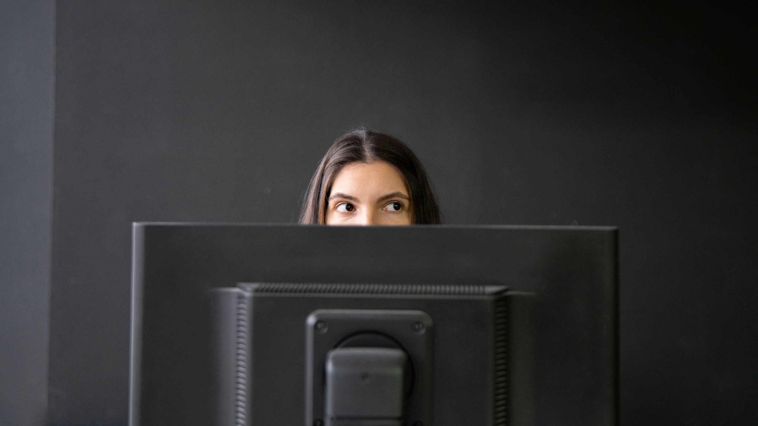 Office Worker Sneaking a Peek Above Laptop in a Modern Workspace During Daytime, hiding from boss.