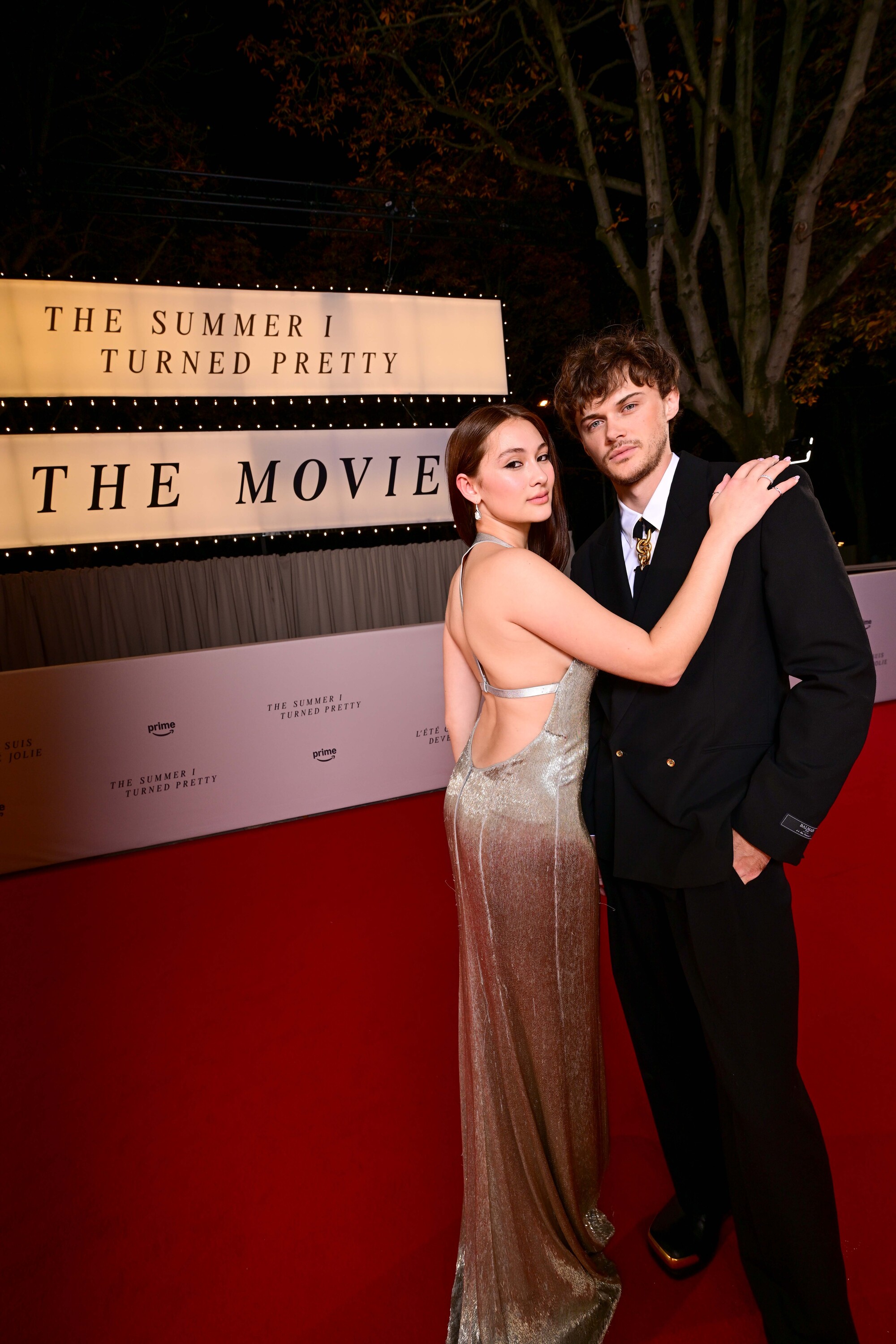 Lola Tung and Christopher Briney pose next to a sign reading 'The Summer I Turned Pretty: The Movie'