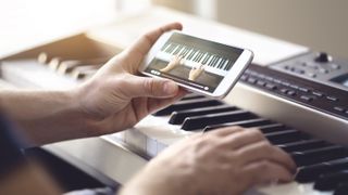 Person sat at a digital piano viewing a lesson on their smartphone