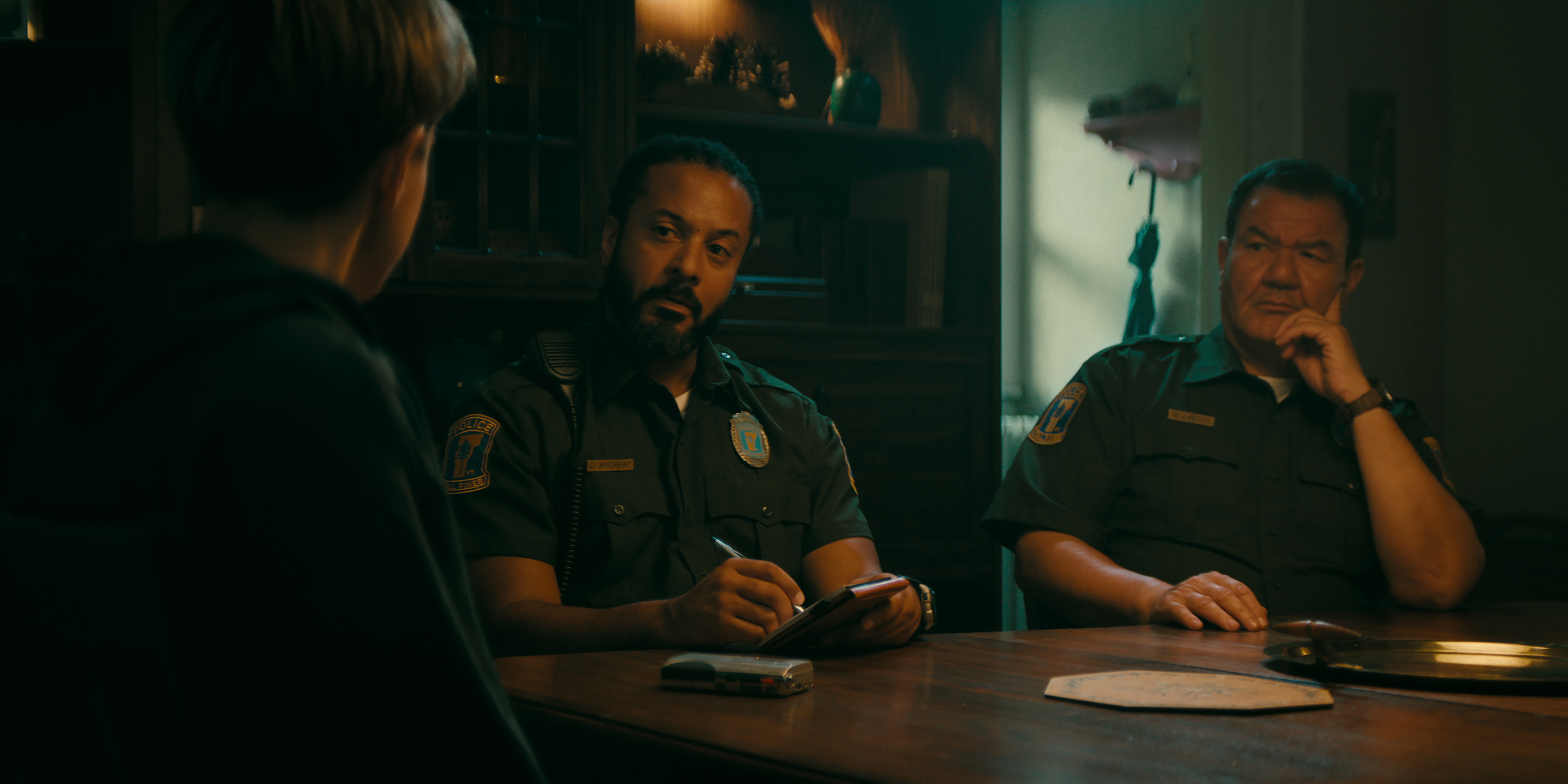 three police officers sit around a table in a still from wayward