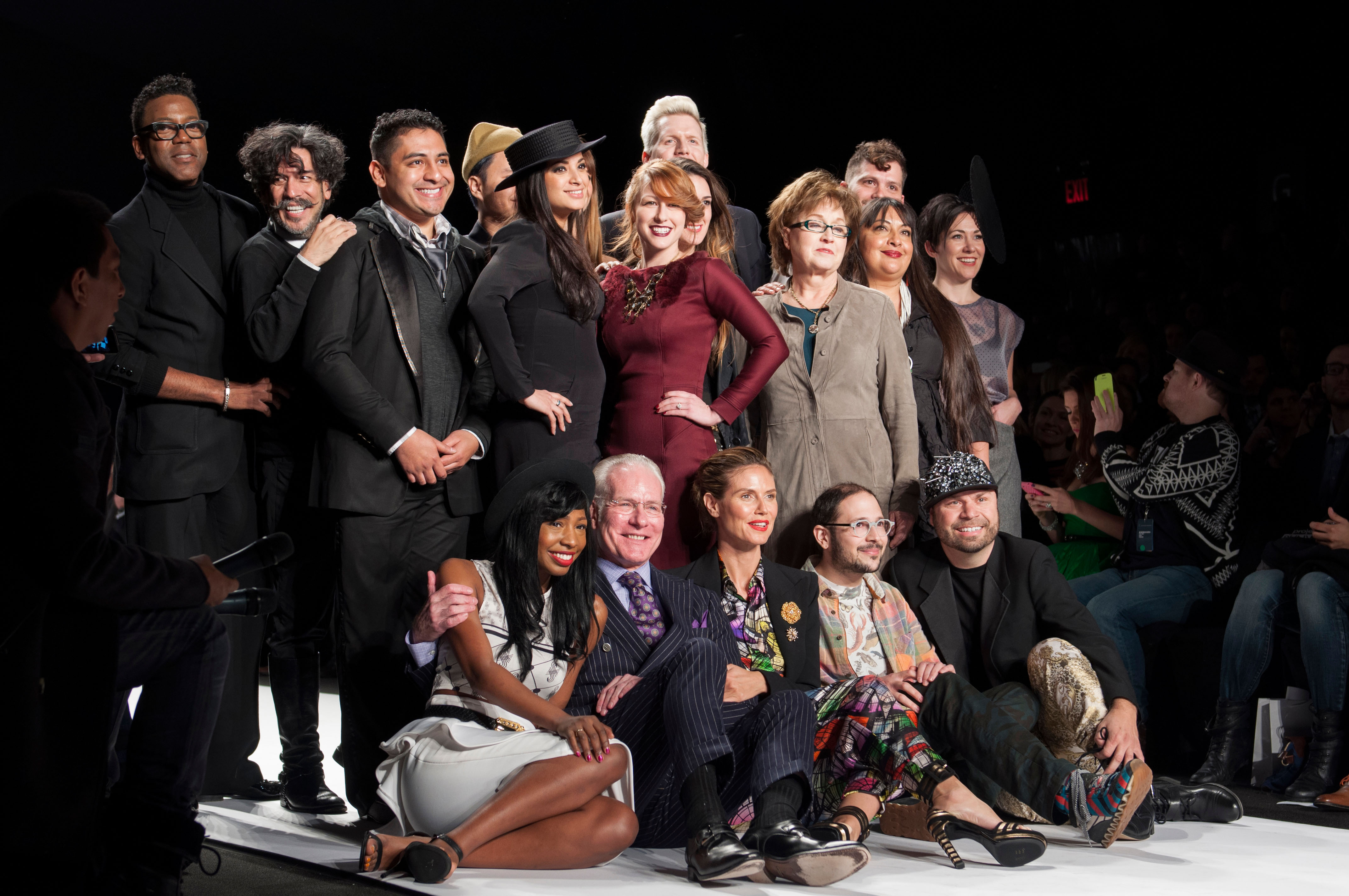 the project runway contestants pose on a runway with the judges after a fashion show