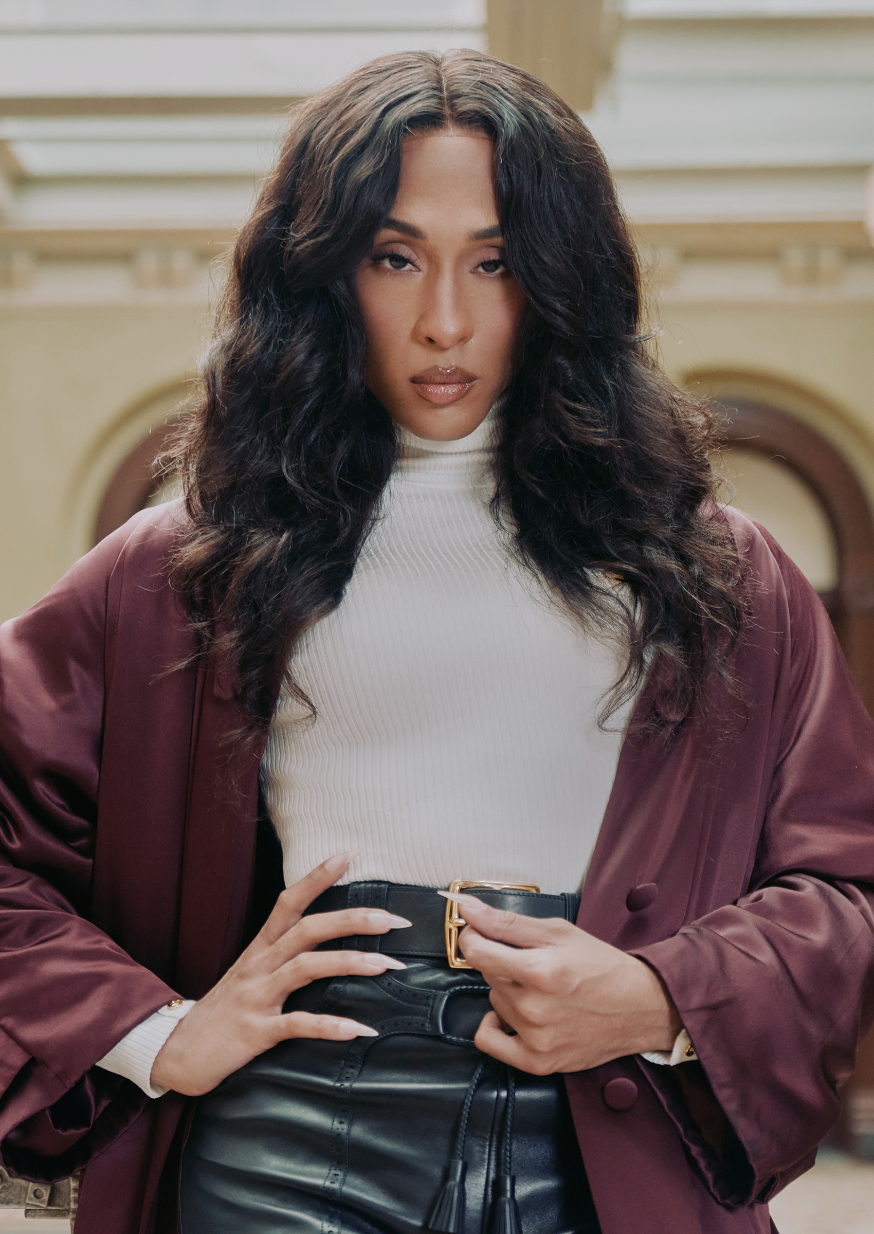 michaela j rodriguez poses in a white turtle neck red leather jacket and black shorts holding her hips