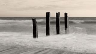 A damaged groyne on a UK beach, the high tide is smashing into it, with the moving water blurred using a long exposure photography technique