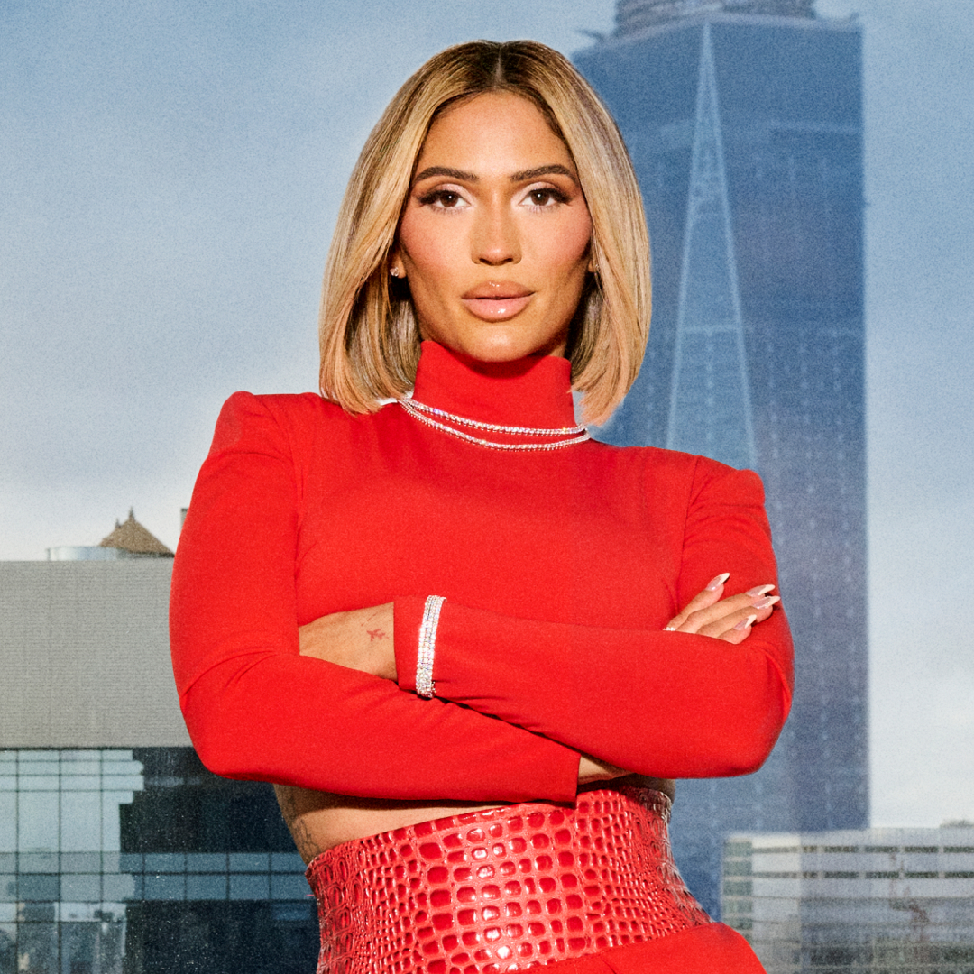 Giselle Meneses-Nunez of Selling the City S1 wearing a red turtle neck and folding her arms