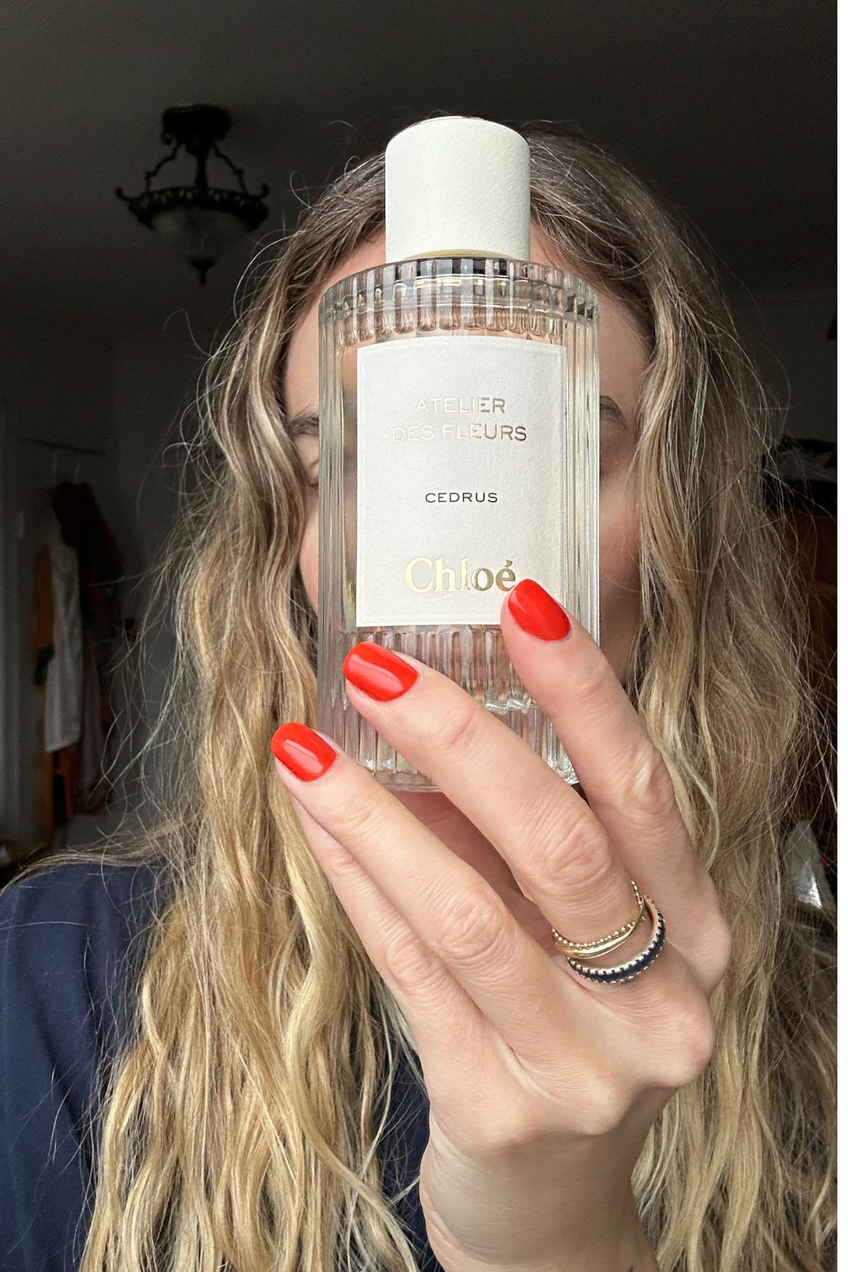 woman holding a glass perfume bottle with red nails