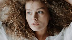 A curly haired woman lying on a bed with her eyes open