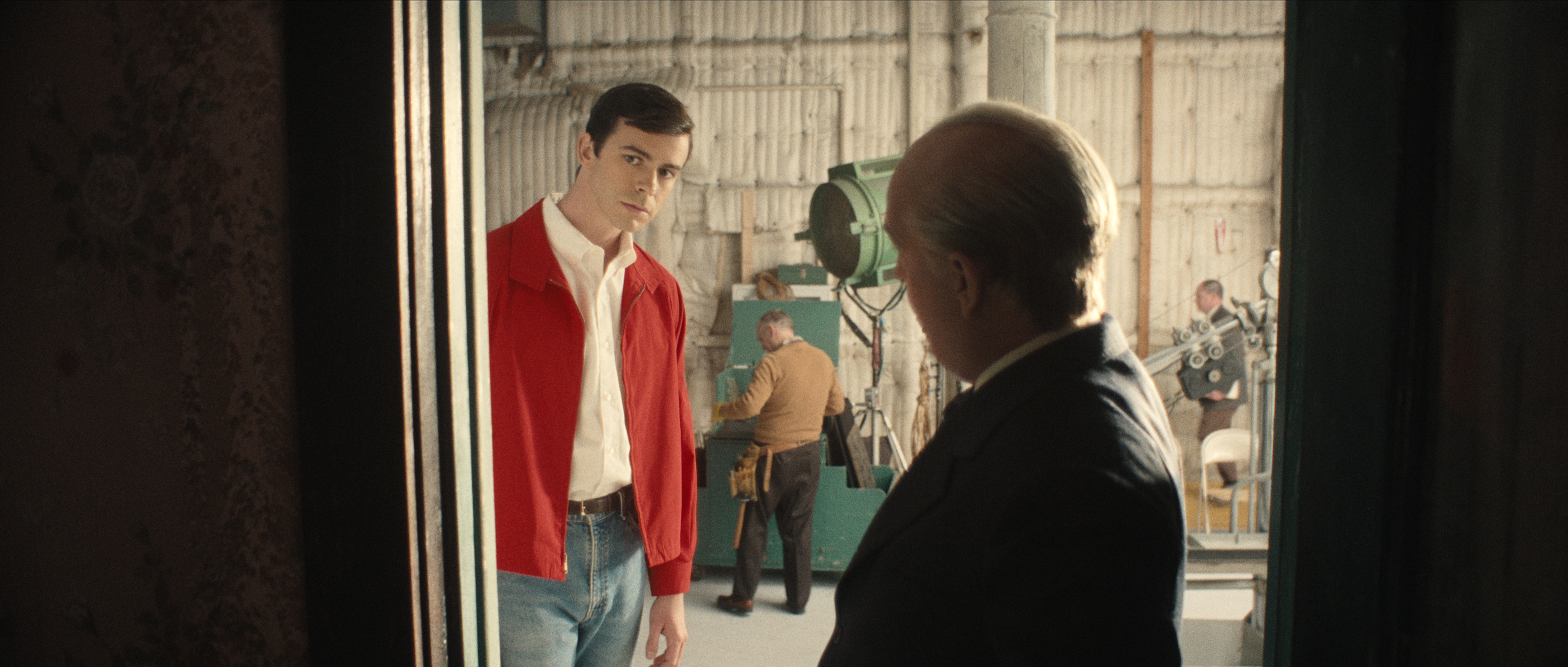Joey Pollari as anthony perkins wearing a red sweater on a movie set talking to hitchcock