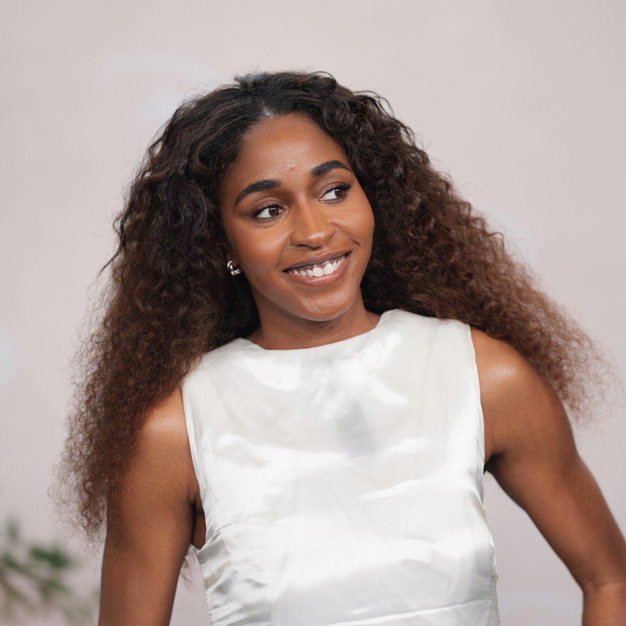 a black woman with long, curly hair wearing a white gown and posing in front of a light background