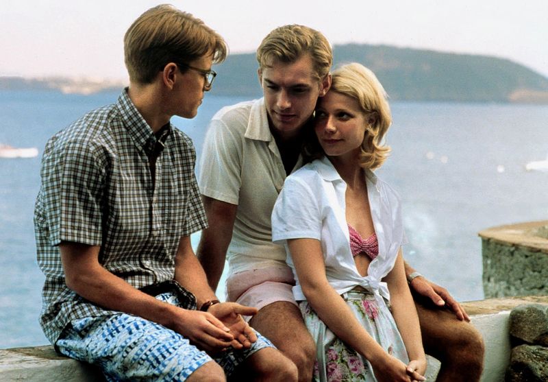 the cast of the talented mr. ripley sitting on a ledge of a rooftop by the ocean