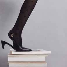 A pair of black kitten heel slingbacks worn with tights on a stack of books.