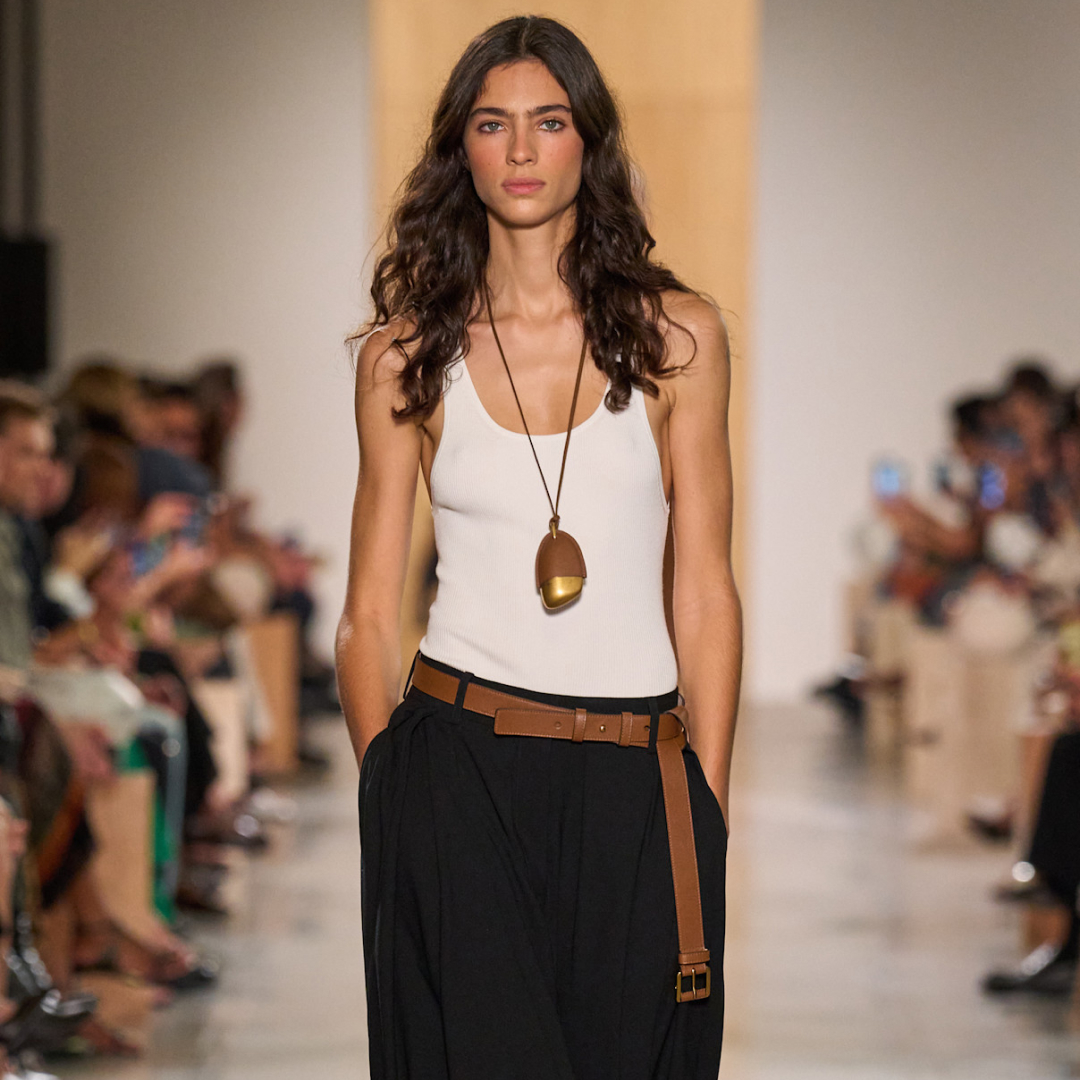 Michael Kors spring 2026 look model wearing white tank top, pendant necklace, brown belt, and black pants 