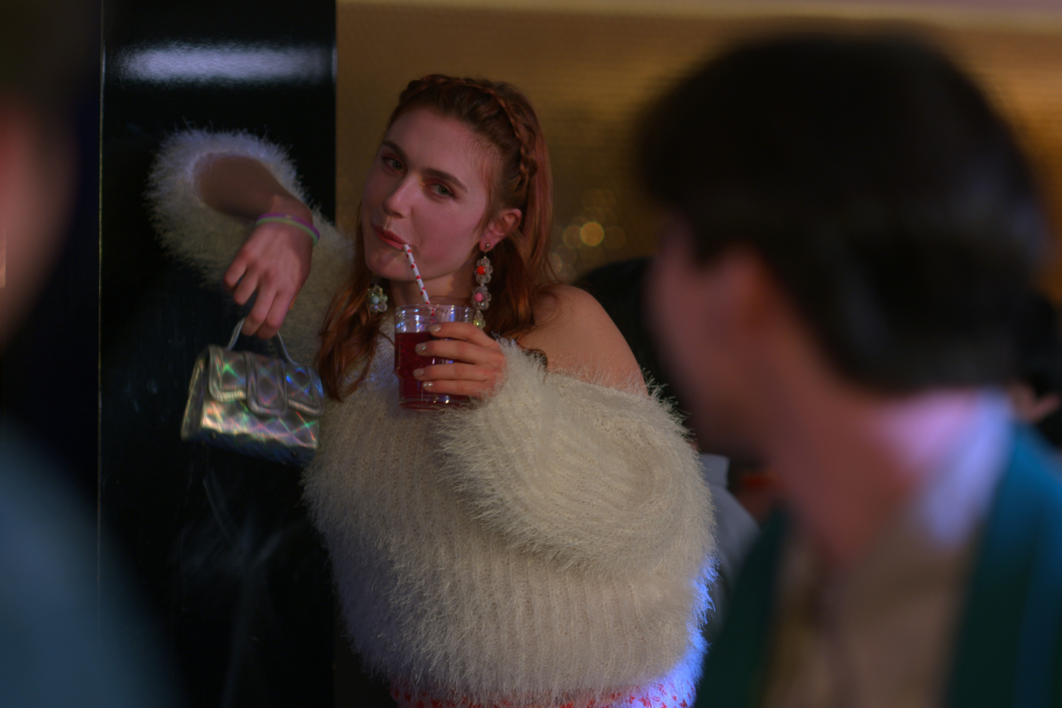 Jocelyn Shelfo wears a furry sweater and sips a drink at a party in a still from xo kitty