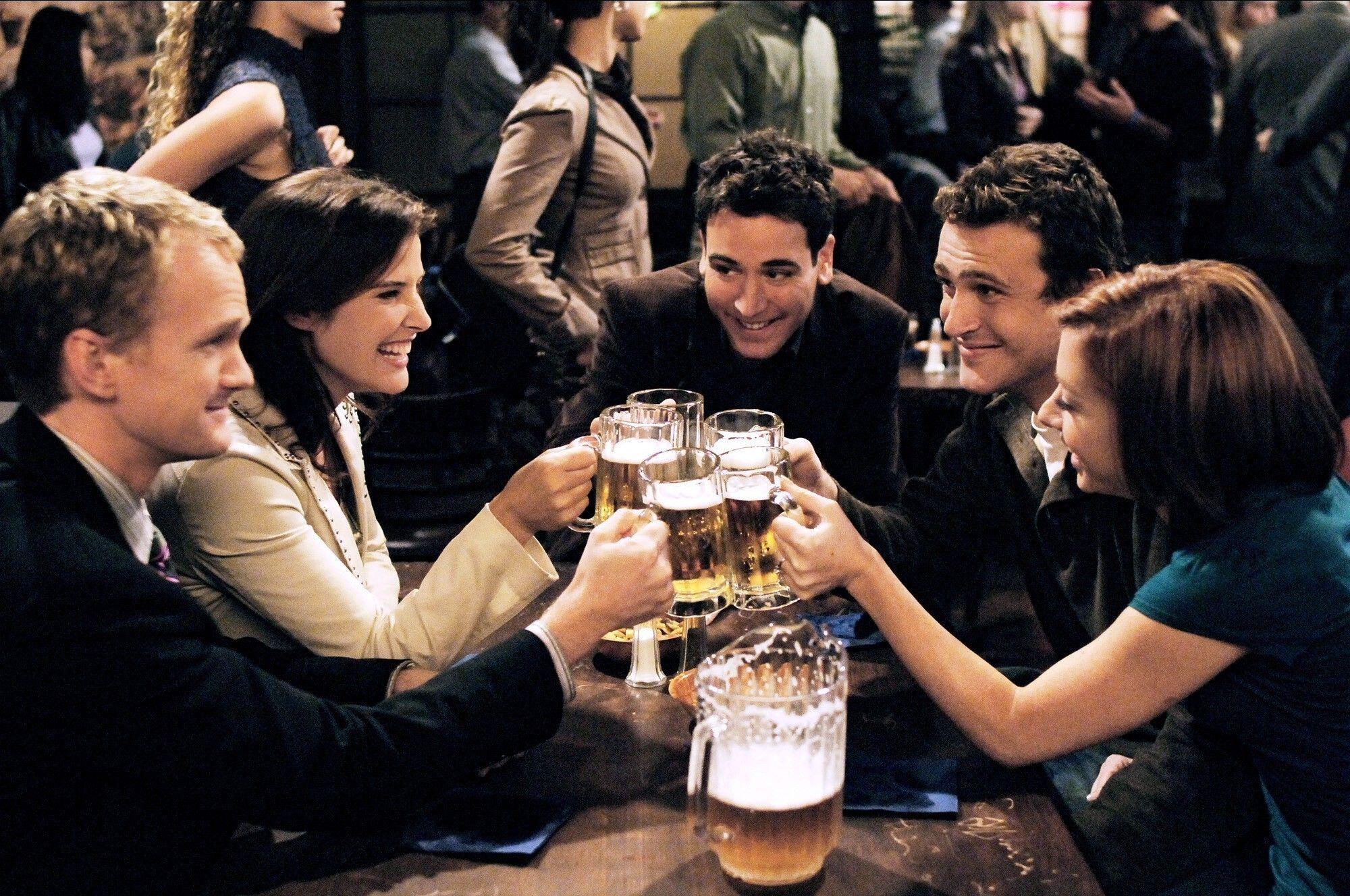 the cast of how i met your mother smiles and cheers beers in a bar
