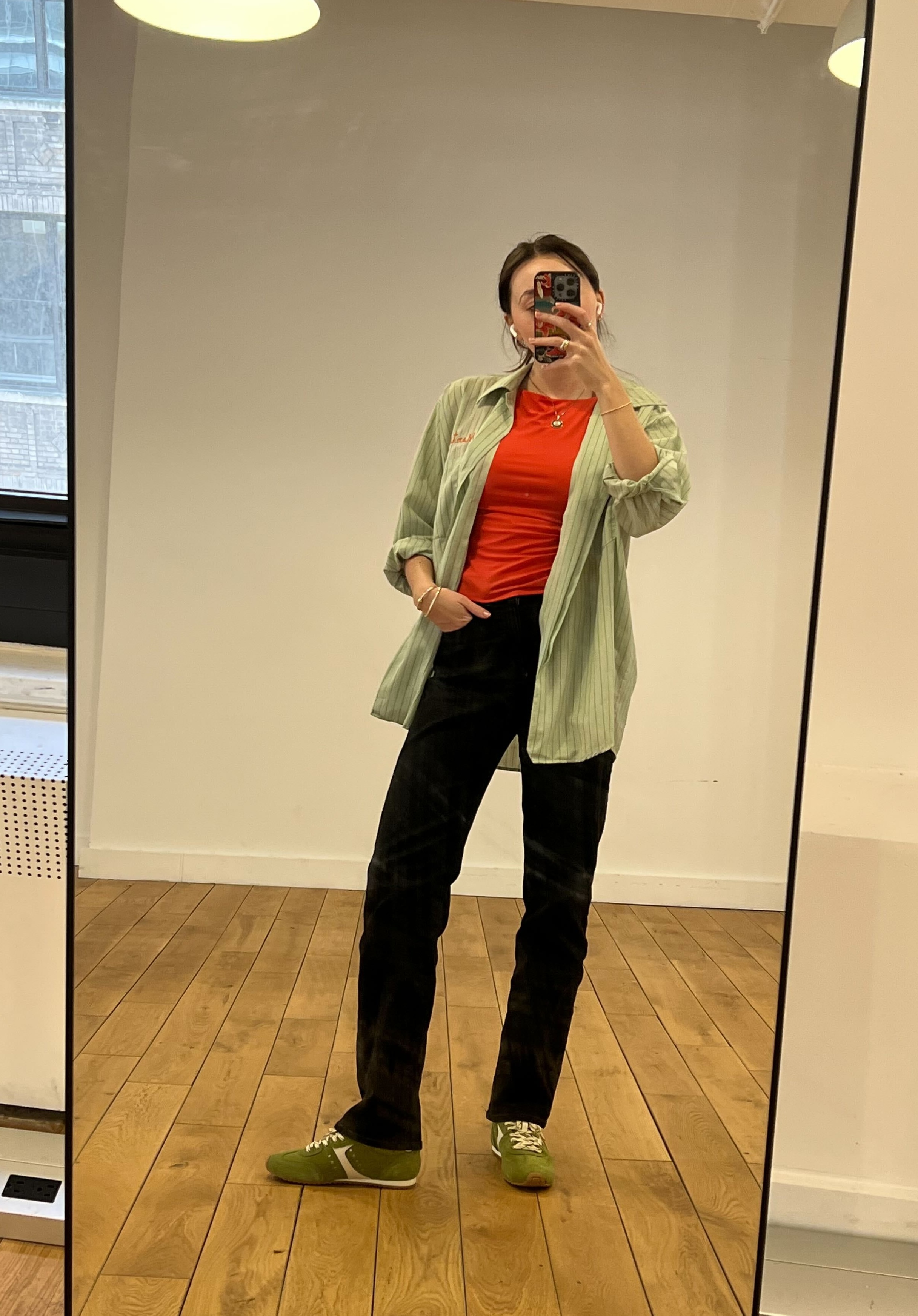 Emma Childs wearing Larroud&amp;eacute;&#039;s Stella Sneaker in Seaweed Suede and Ivory Leather with black jeans, an orange top, and green button-down shirt.