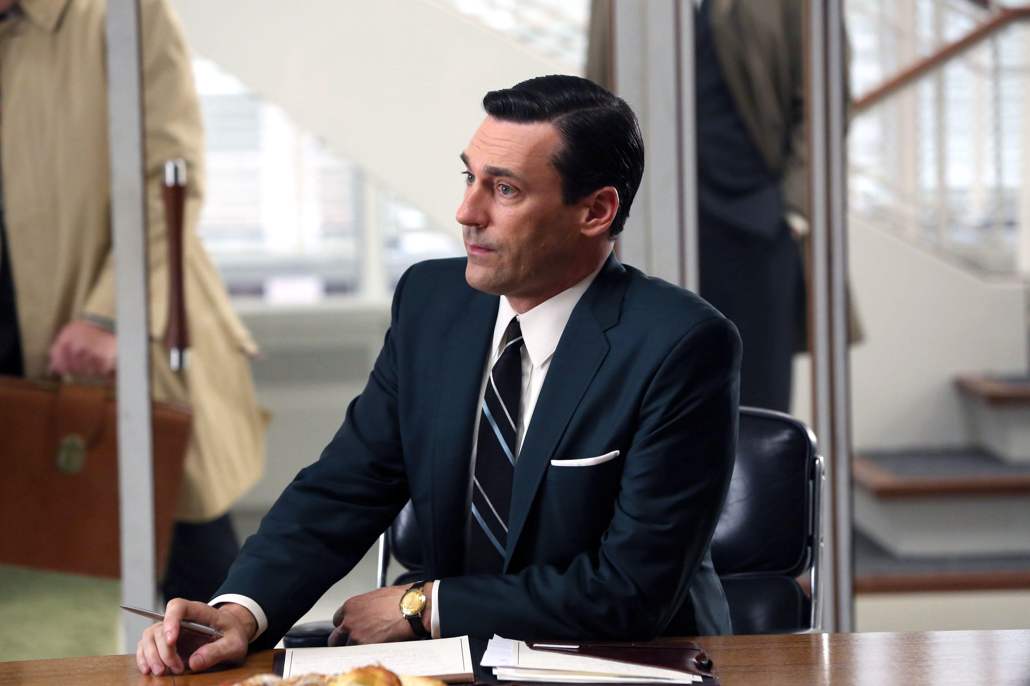 don draper wearing a suit sitting at a conference room desk in mad men