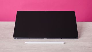The Samsung Galaxy Tab S10 FE sat on a table behind the S Pen and in front of a pink background.