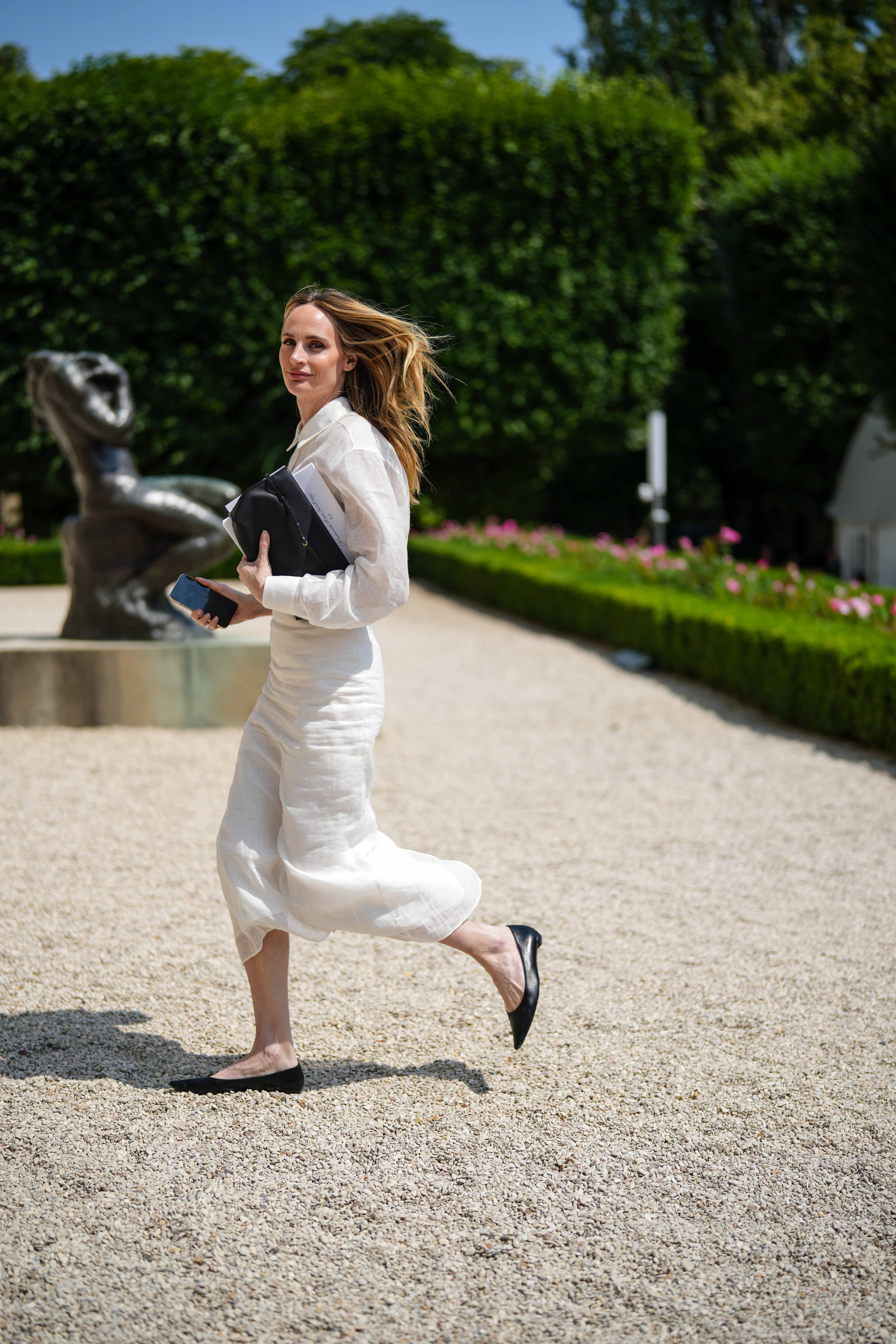 A guest wears a white latte linen shirt, a white linen matching midi skirt, a black shiny leather clutch, black shiny leather pointed ballerinas , outside Dior , during the Haute Couture Fall/Winter 2023/2024 as part of Paris Fashion Week on July 03, 2023 in Paris, France.