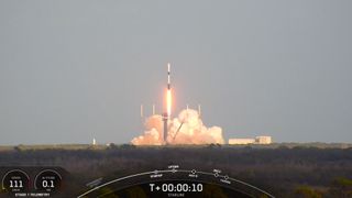 a black-and-white spacex falcon 9 rocket launches into a blue sky.