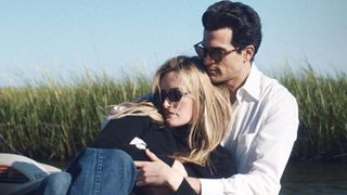 Caroline sits on John's lap with his arms wrapped around her in FX's Love Story 