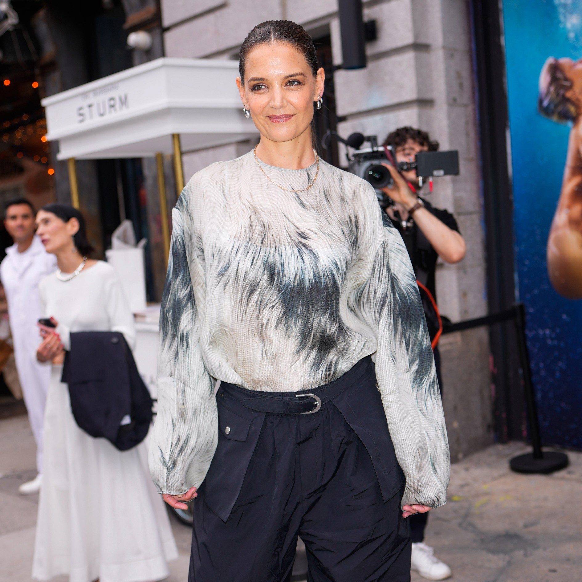 a woman in a faux fur printed blouse and black trousers being photographed by the paparazzi
