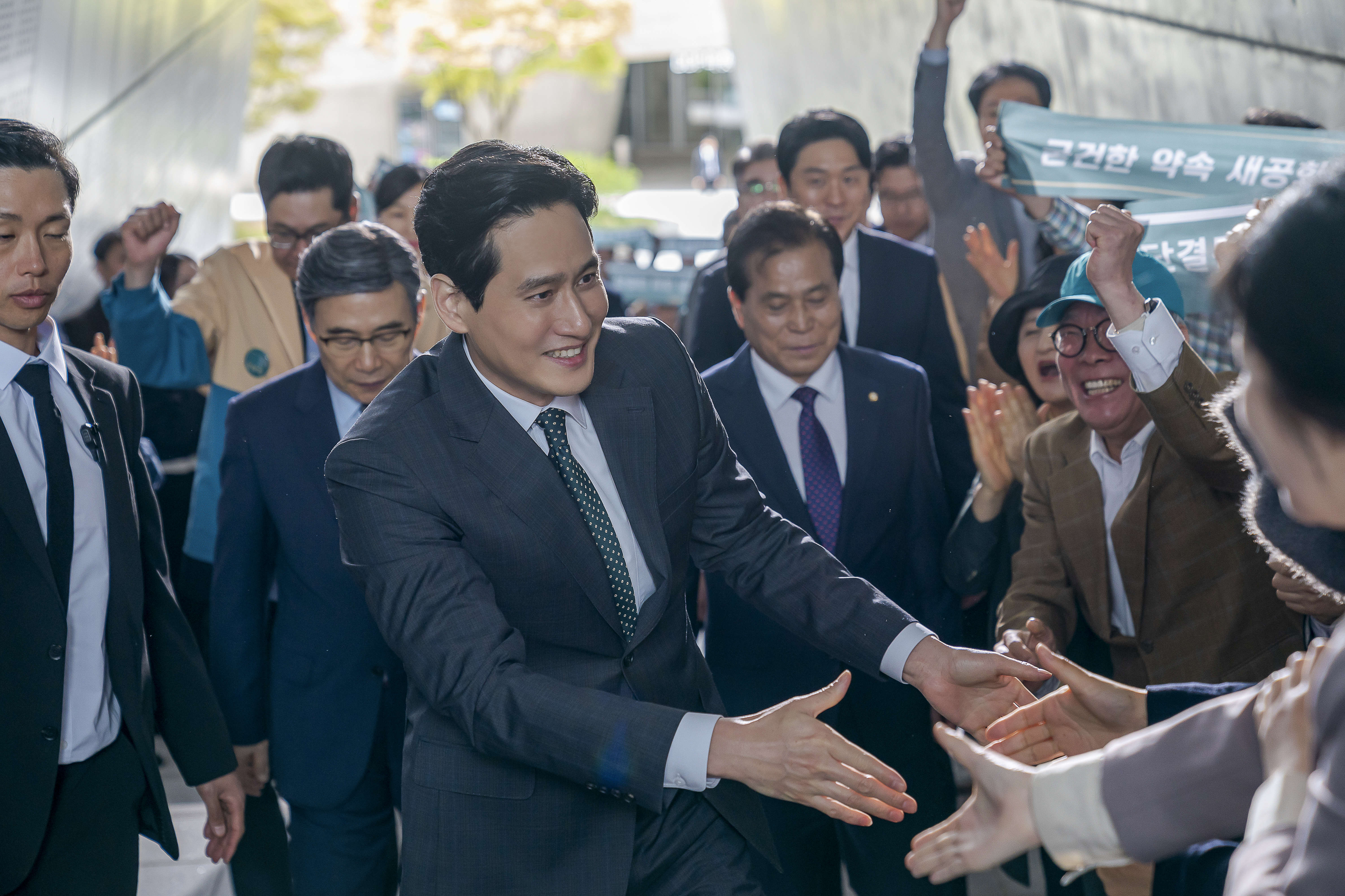 Park Hae-joon wears a suit and greets people in a ground in 'Tempest.'