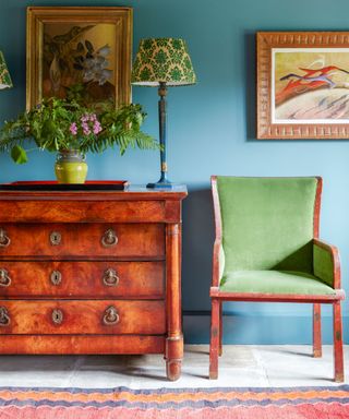 Blue living room with green chair, wooden sideboard, artwork on walls