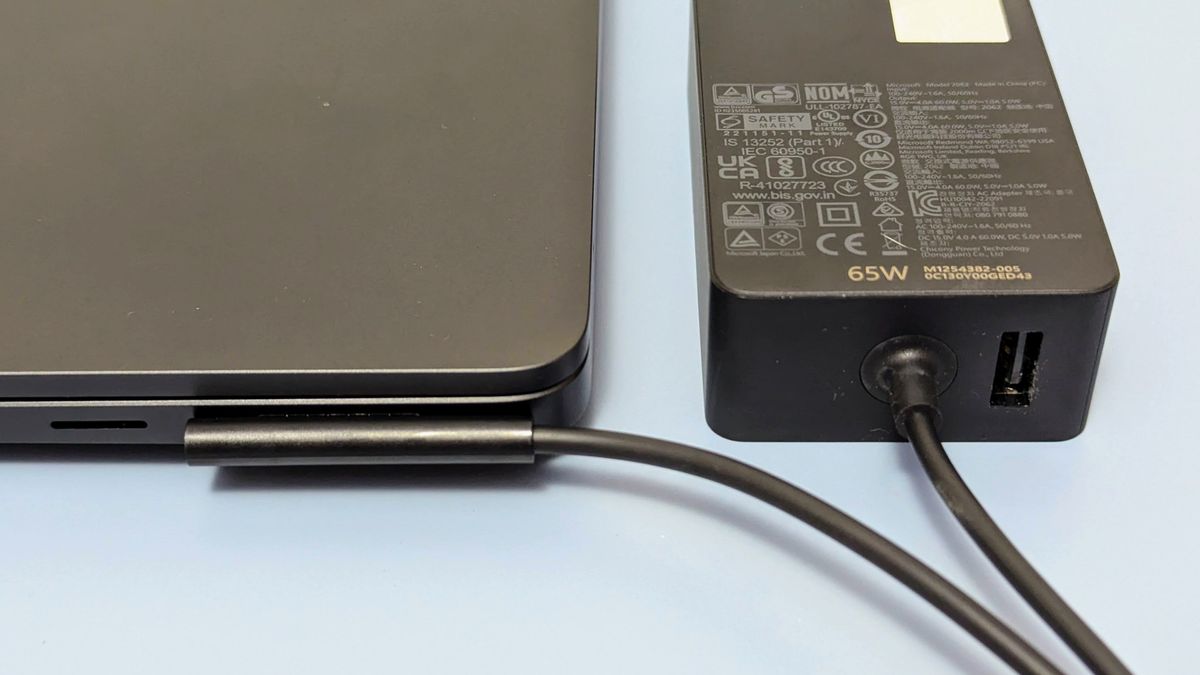 Close up of magnetic charging port and connector with power brick beside the Microsoft Surface Laptop 7