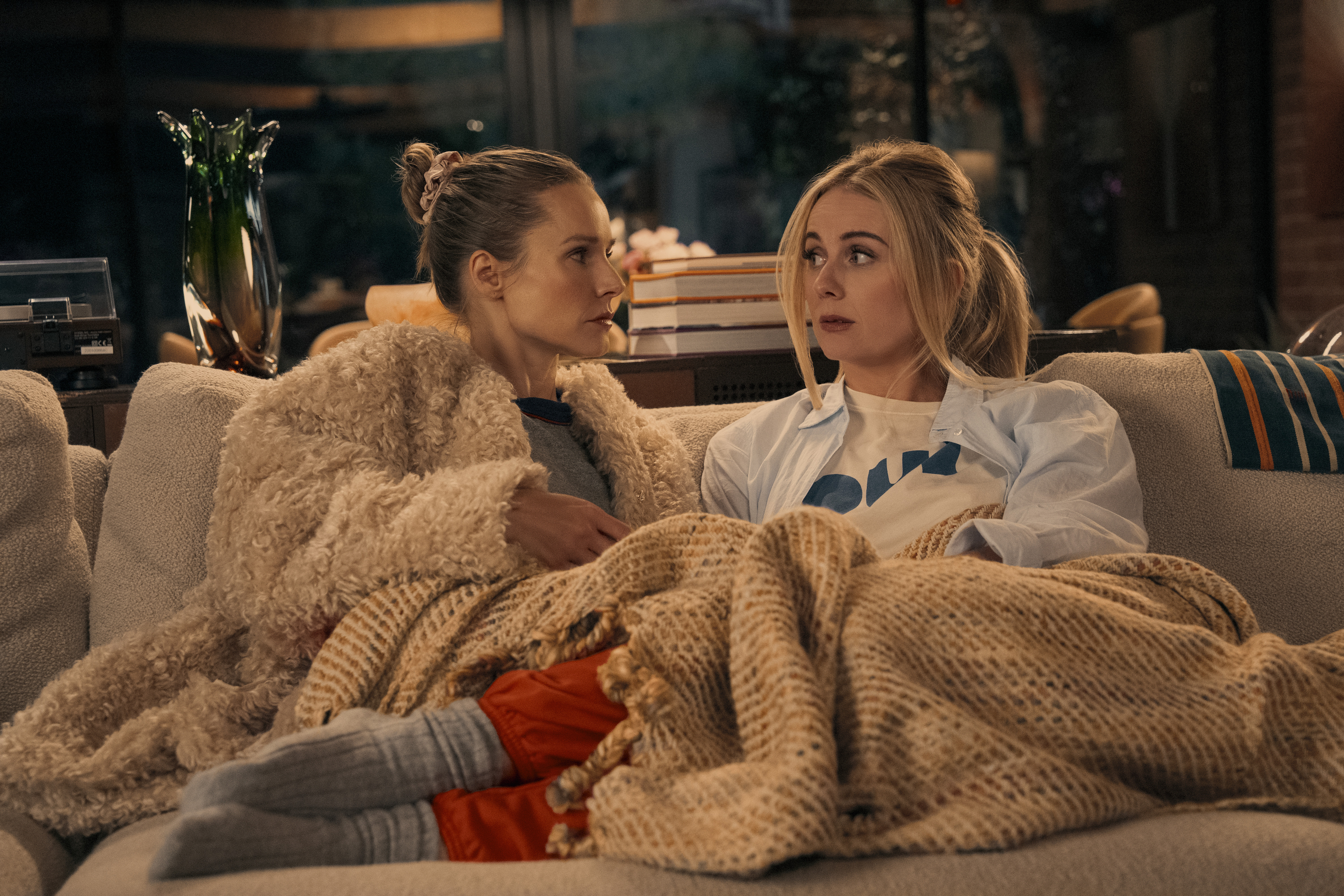 justine lupe and kristen bell sitting on a couch in blankets in nobody wants this season 2