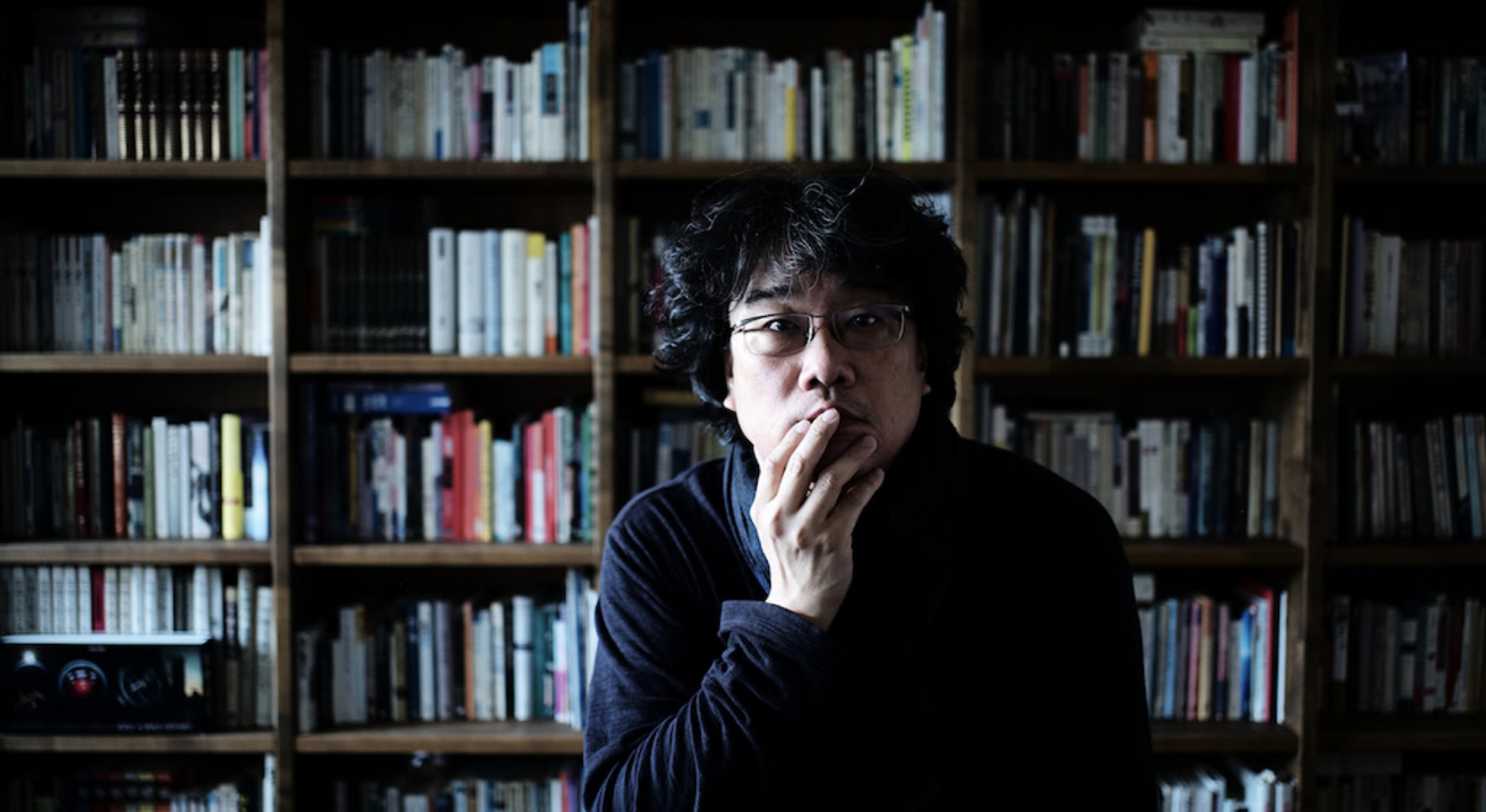 bong joon-ho holding his fingers on his chin sitting in front of a shelf of books in the documentary yellow door