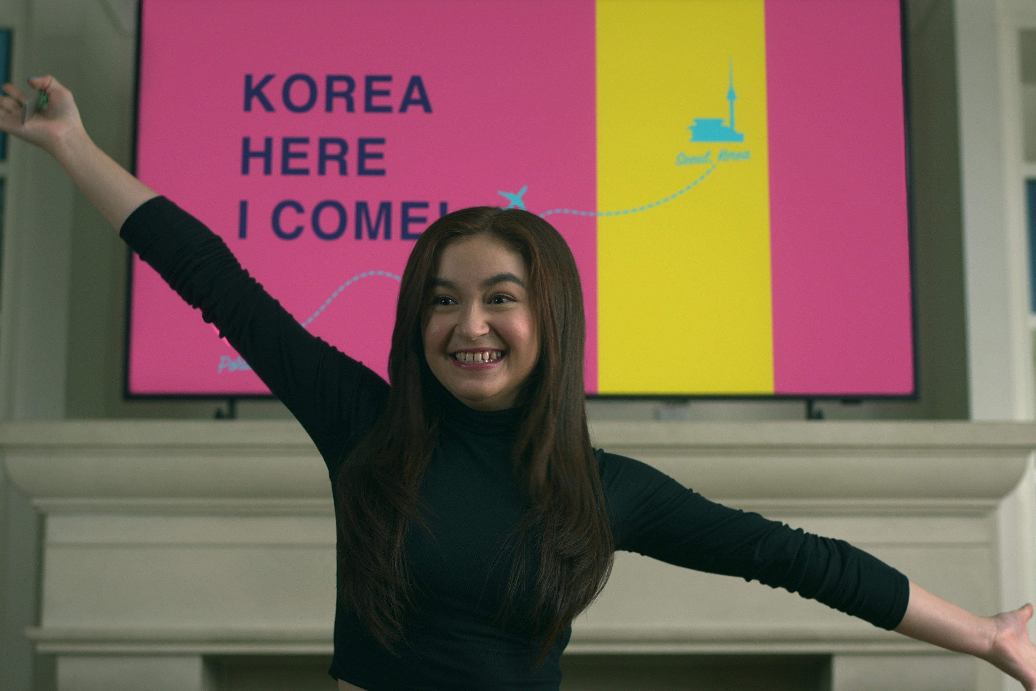 anna cathcart smiling and standing in front of a sign that says korea here i come in xo kitty