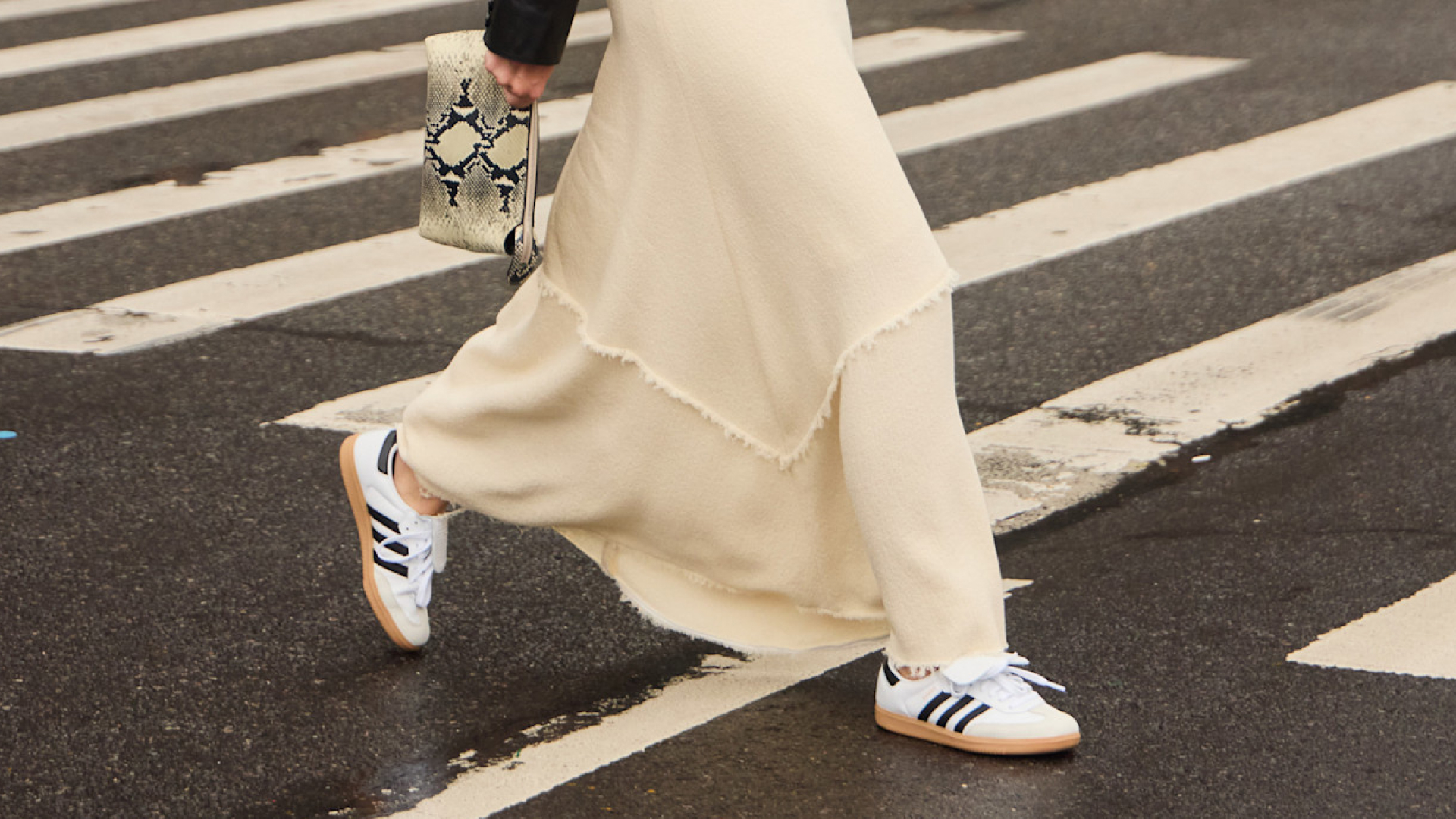 women crossing the street wearing long white skirt, adidas sneakers and carrying snakeskin bag