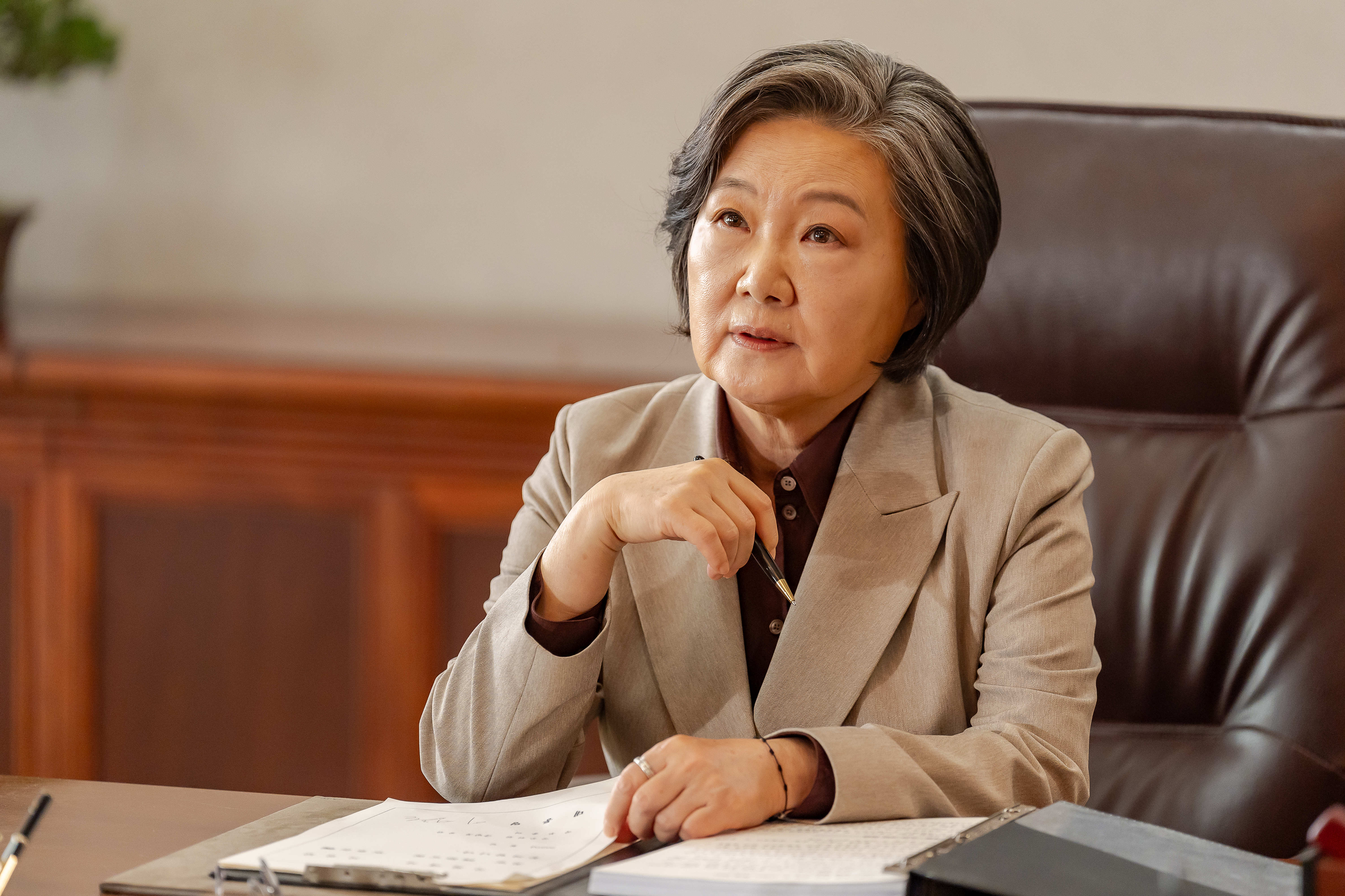 Kim Hae-sook wears a tan stui and sits at a desk in 'Tempest.'