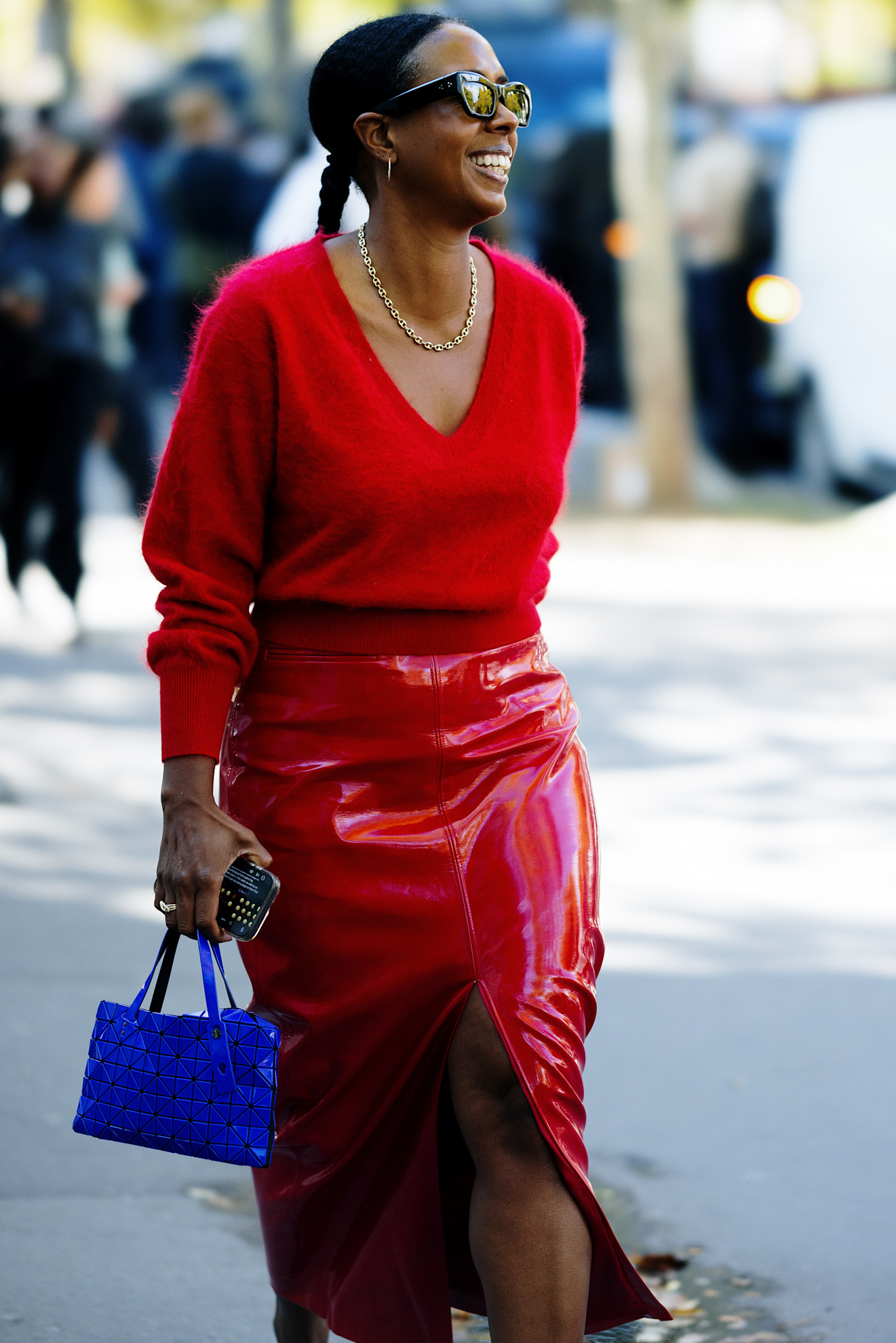 a woman with a red leather skirt, red sweater, blue bag and dark sunglasses