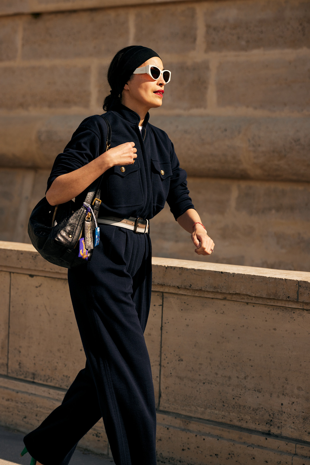 a woman with an all black outfit, white sunglasses, dark hair in a bun and red lipstick
