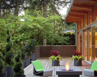 A raised deck area with green chairs, a fire pit and foliage