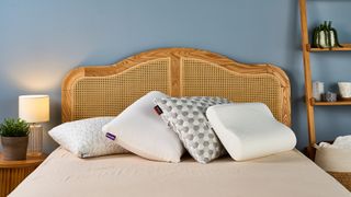 A stack of four pillows resting against each other at the head of a bed in a warmly lit room