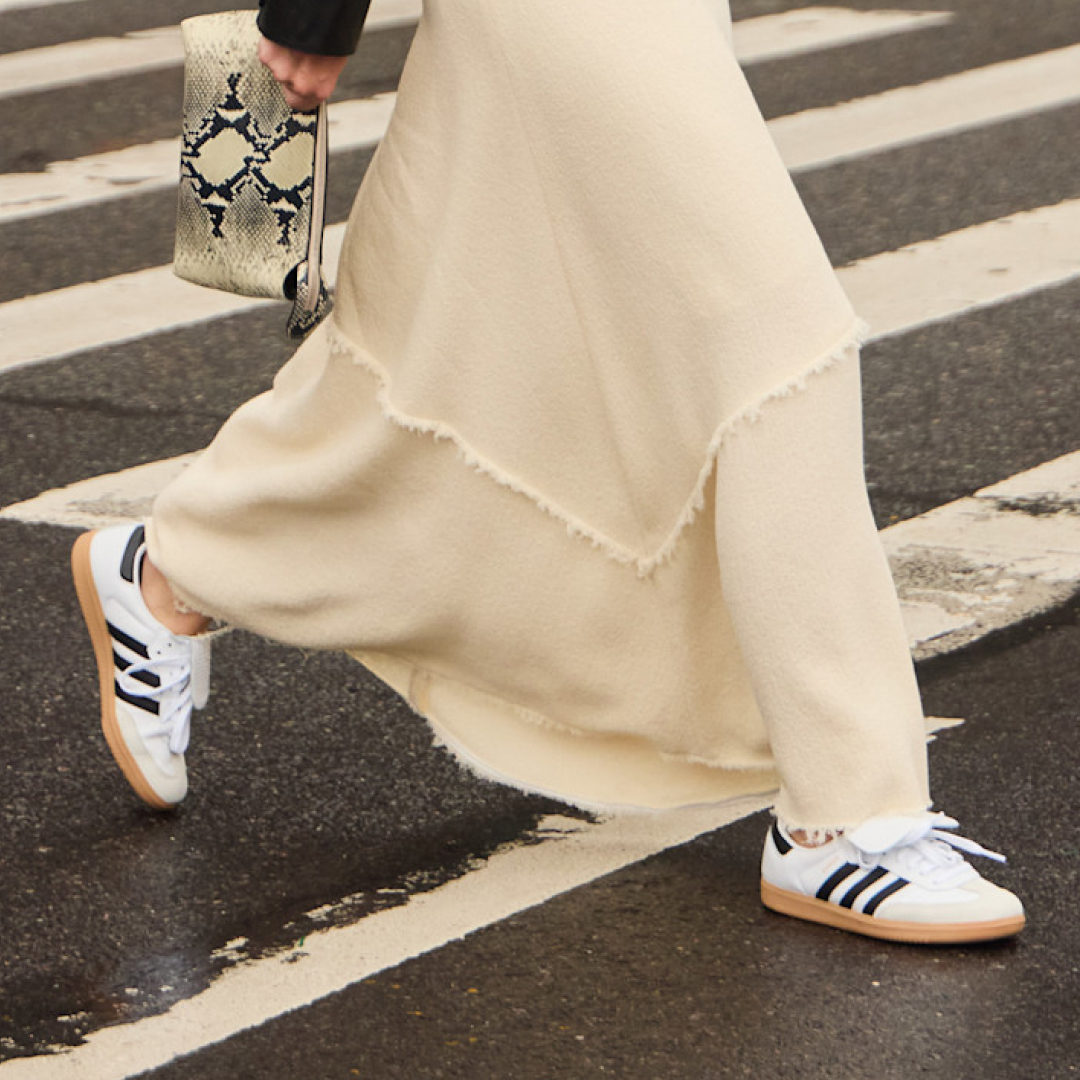 women crossing the street wearing long white skirt, adidas sneakers and carrying snakeskin bag