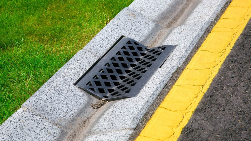Water flowing into a drain next to a lawn