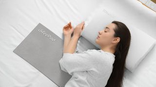 A woman lies in bed with an iSleePad placed on the mattress