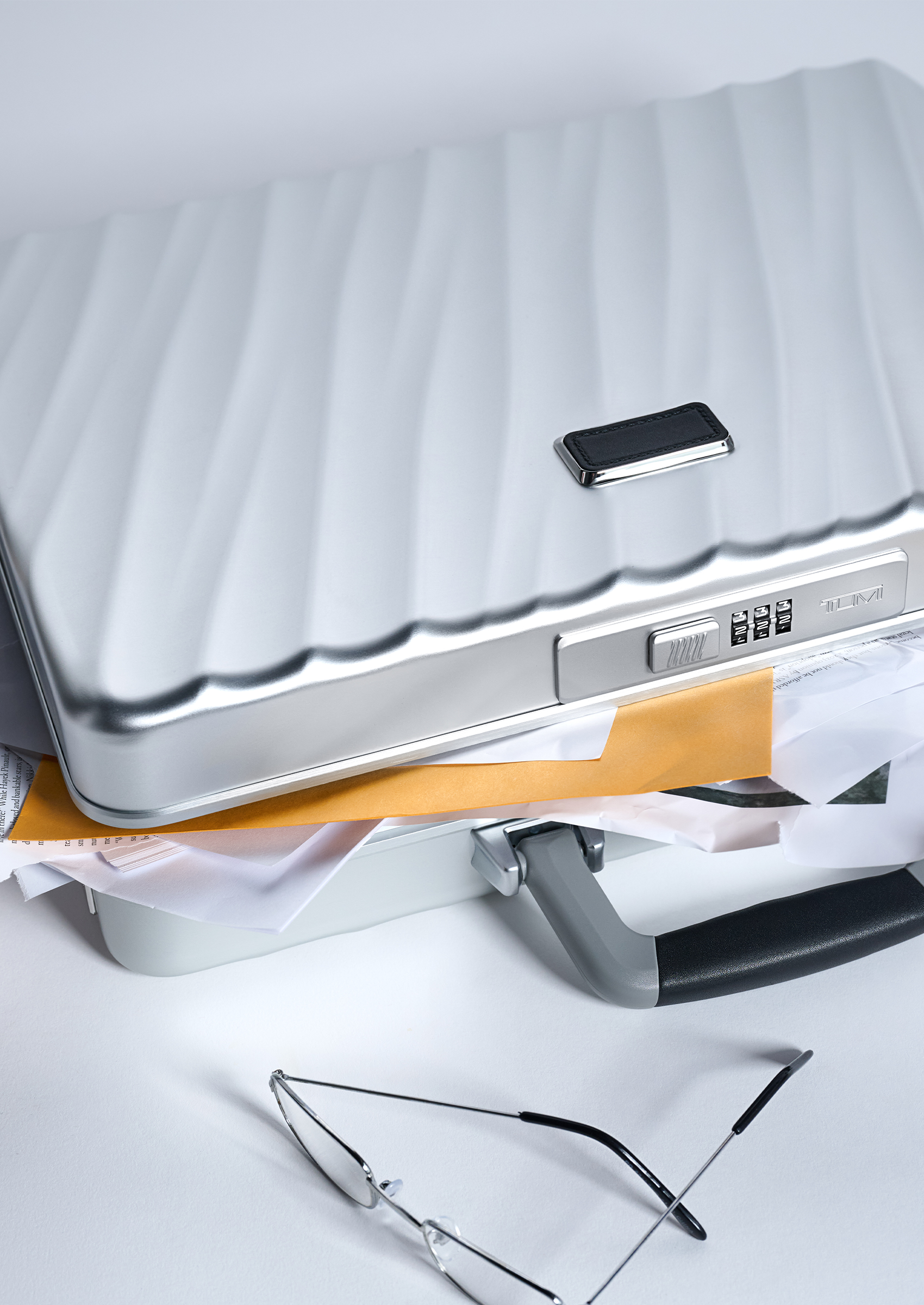 A silver Tumi briefcase with papers and files sticking out of the top