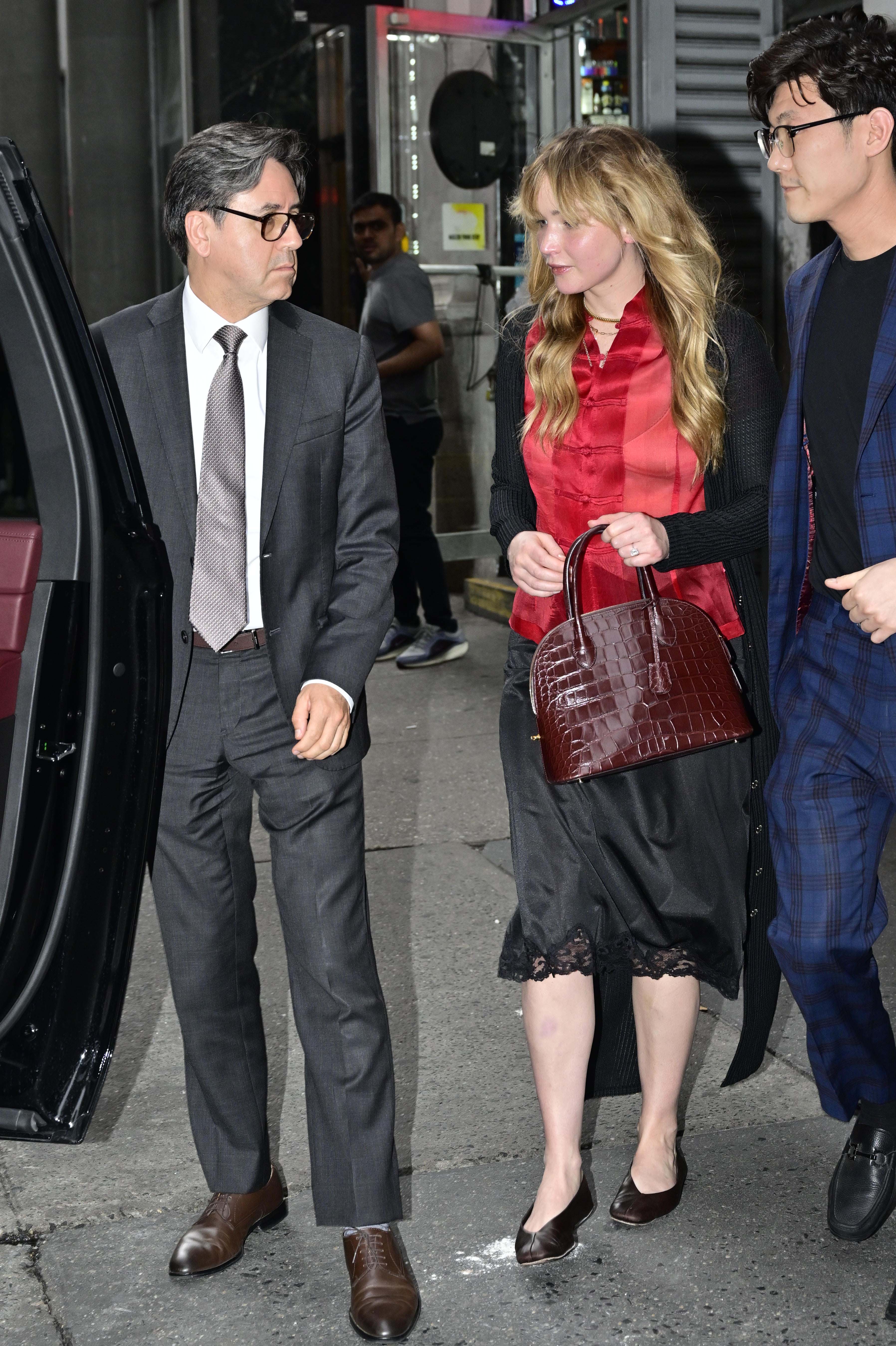 Jennifer Lawrence wears a black lace skirt with a red silk shirt and flat pumps