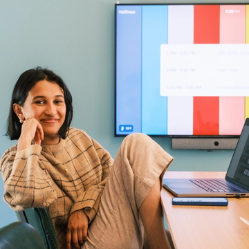 A Figmate smiling at the camera with a laptop on a table