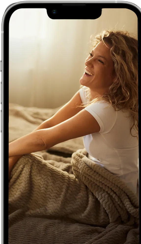 A visual representation of a mobile device with a bed background displaying an image of a woman sitting and smiling.