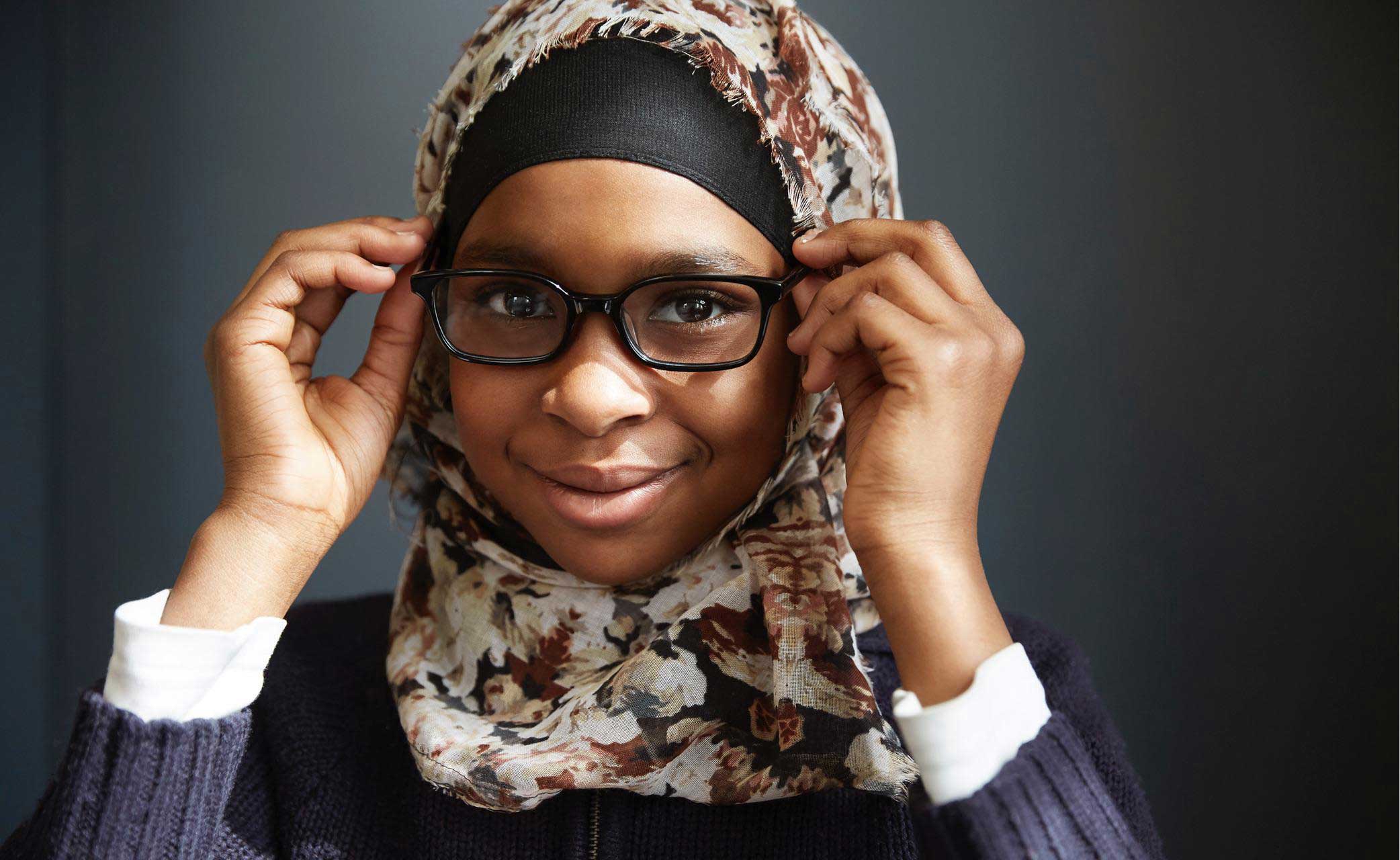 Person smiling, adjusting glasses, wearing floral hijab and sweater