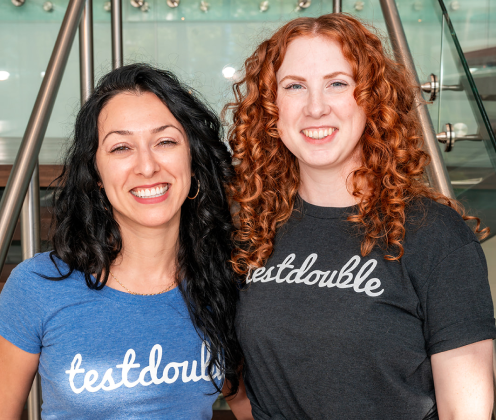 Two test double employees wearing test double t-shirts embrace and smile at the camera.