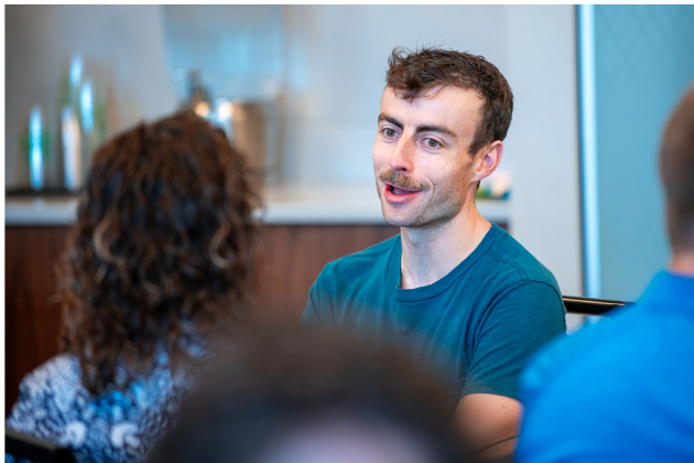 A person laughs at the camera in a group setting with a group of people.